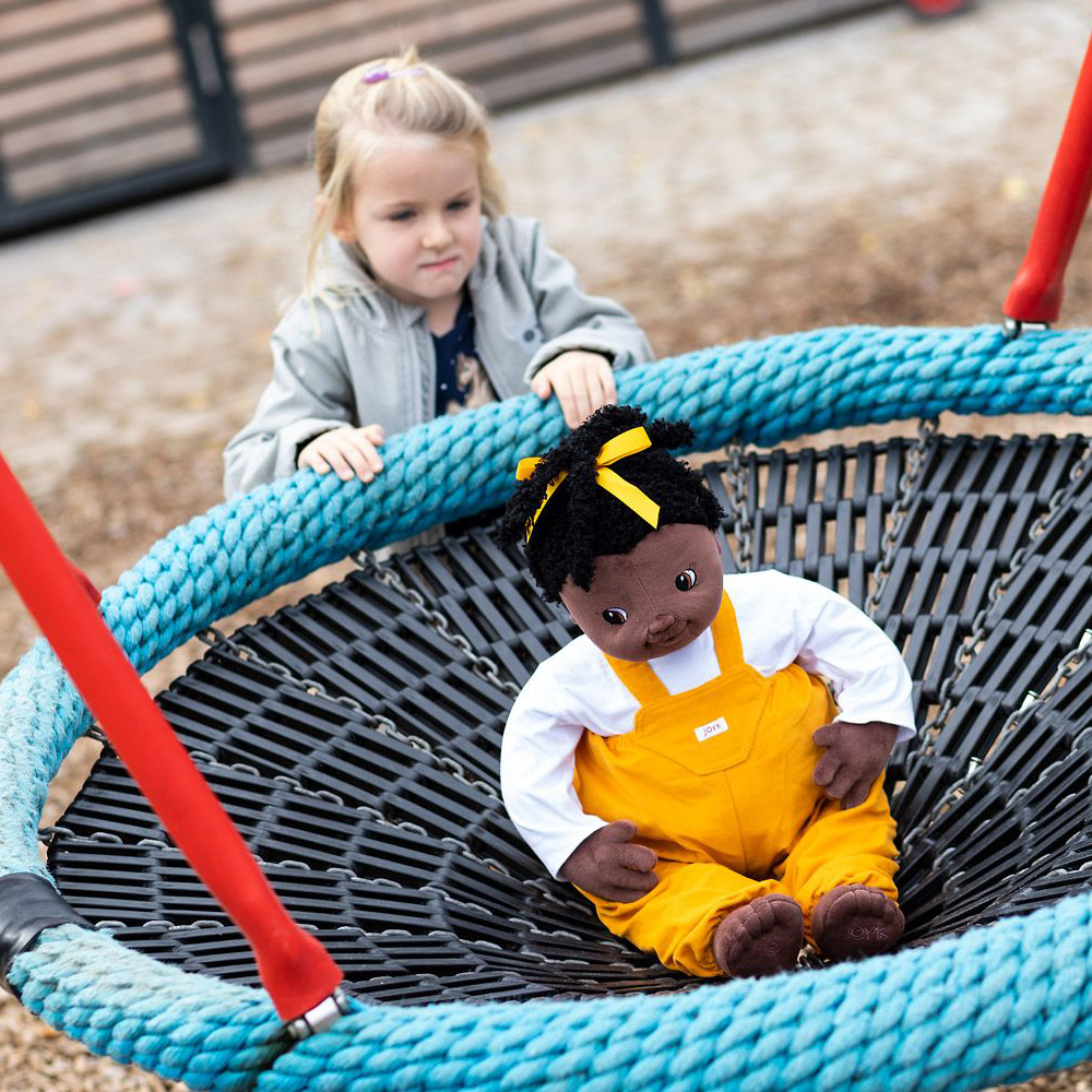 The Joyk empathy doll Sofia sitting in a nest swing on the playground