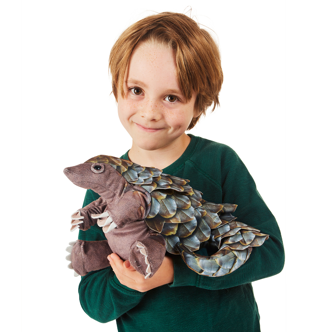 Boy holding a Folkmanis pangolin hand puppet with detailed blue-brown scales and a movable mouth against a white background