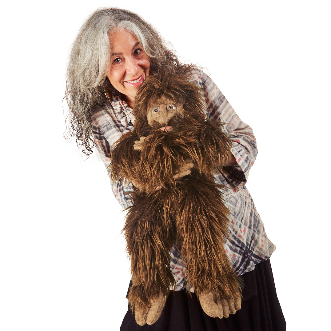 Folkmanis Bigfoot hand puppet with shaggy brown fur, held by a smiling woman, full-body view on white background
