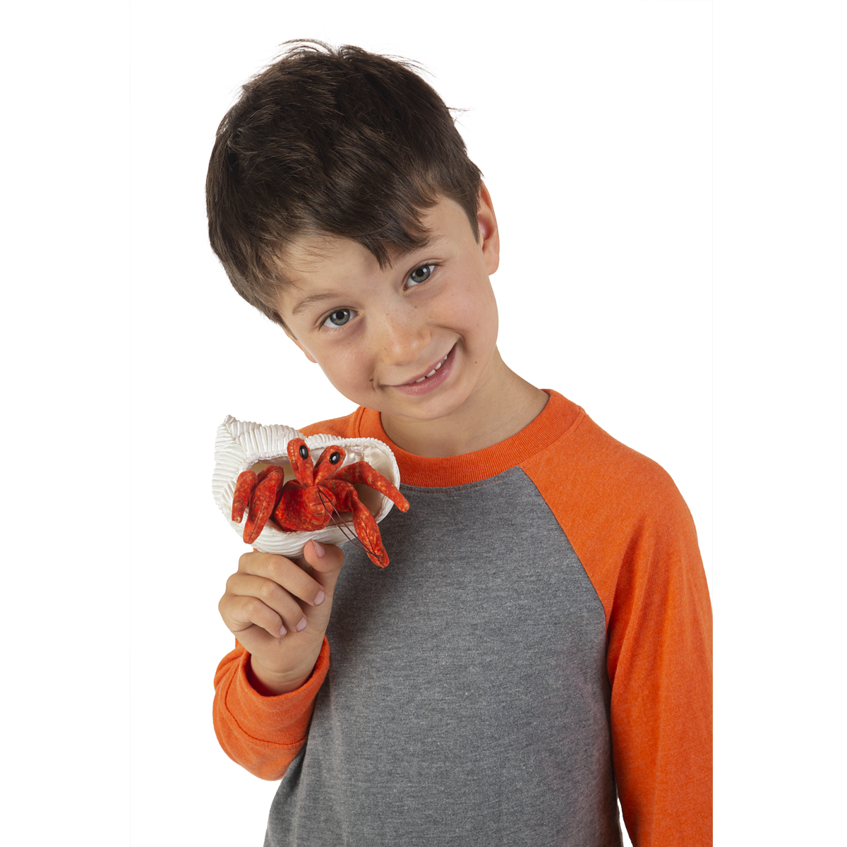 Boy holding a Folkmanis mini hermit crab finger puppet in orange-red with a white shell casing up to the camera