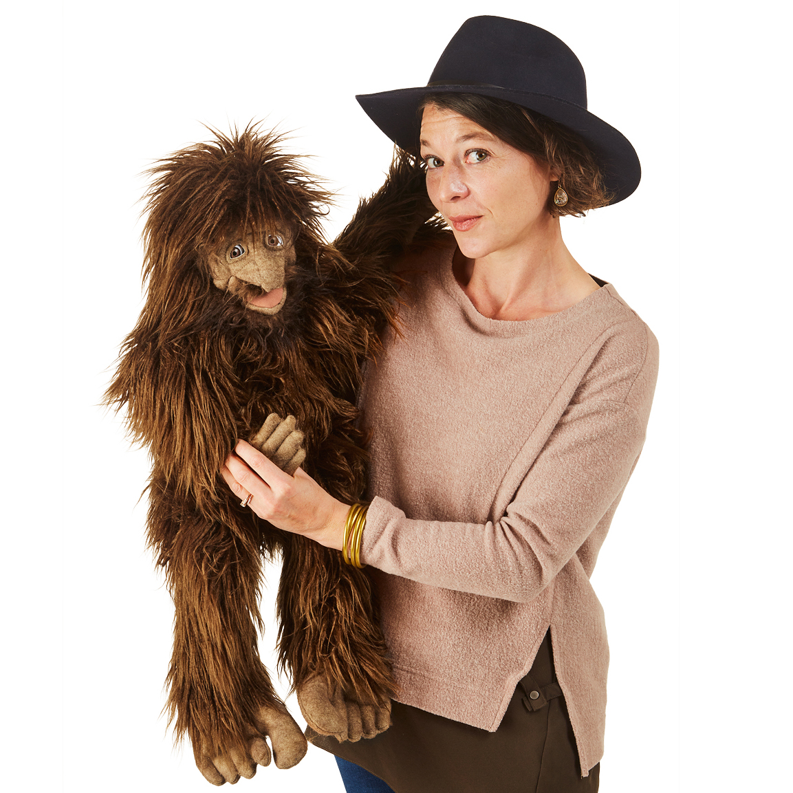Folkmanis Sasquatch hand puppet with shaggy brown fur, operated by a woman wearing a hat, full-body view