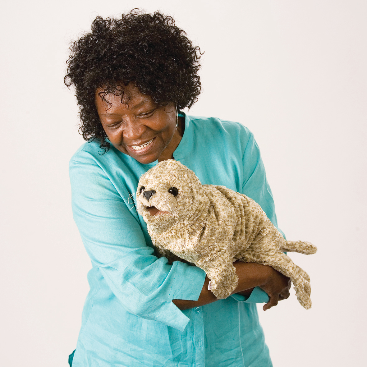 Laughing woman in a teal top cradling the Folkmanis harbor seal baby hand puppet in beige plush