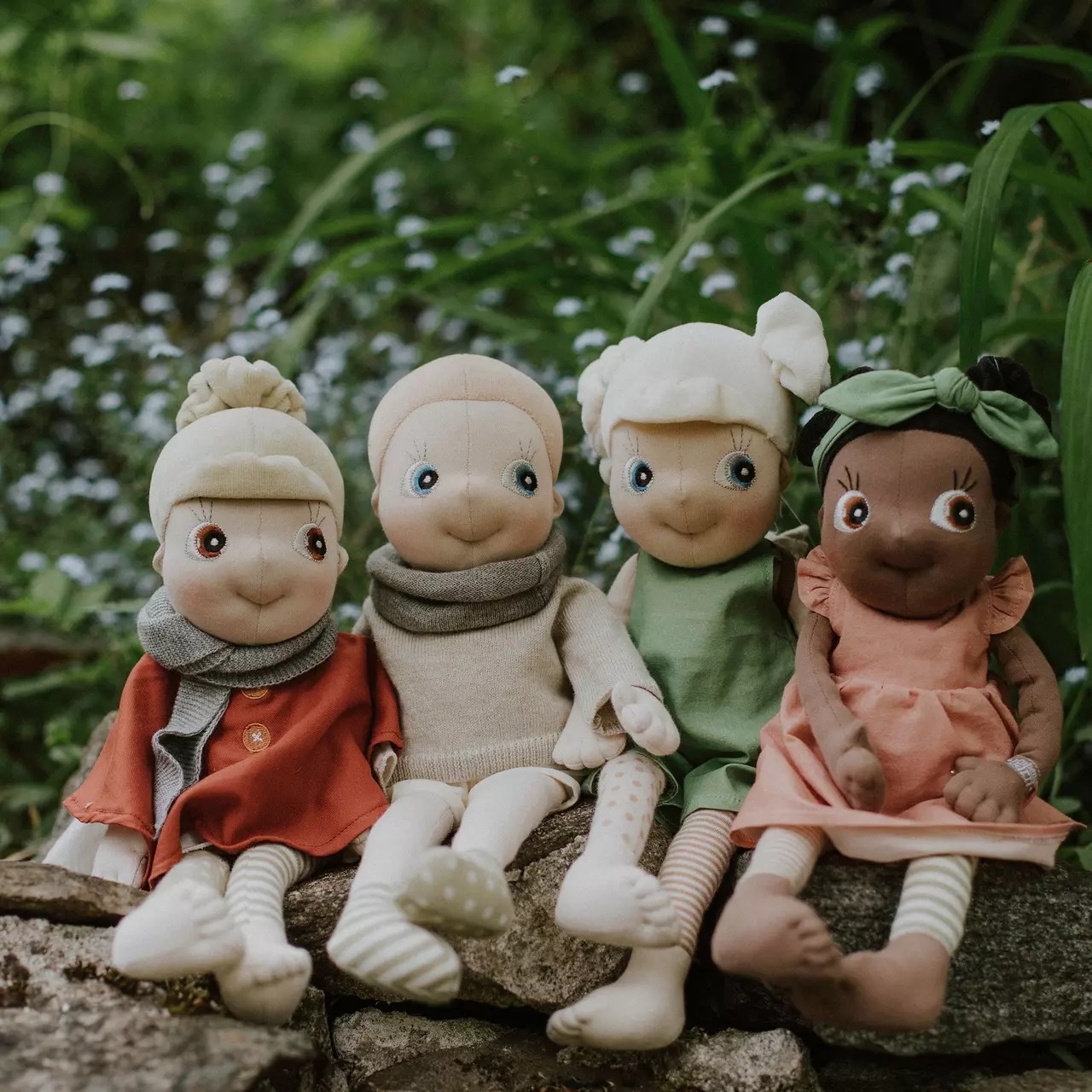 Four Rubens EcoBuds dolls in seasonal outfits on a stone wall, autumn in rust red