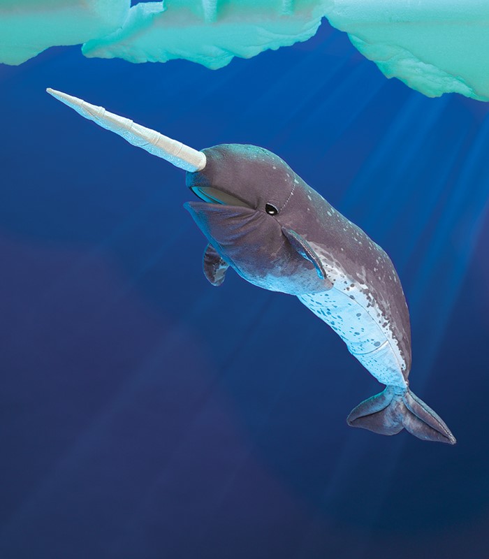 Folkmanis narwhal hand puppet in grey-blue with a long white horn, against a deep blue underwater background