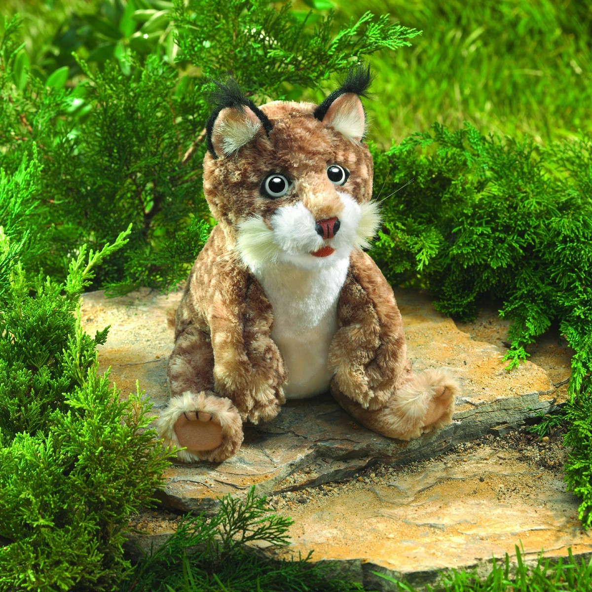 Folkmanis bobcat kitten hand puppet sitting on a stone, brown spotted fur, black ear tufts, white belly, open mouth
