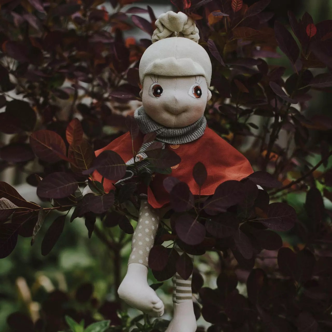Rubens EcoBuds doll in the rust-red autumn poncho among dark autumn leaves