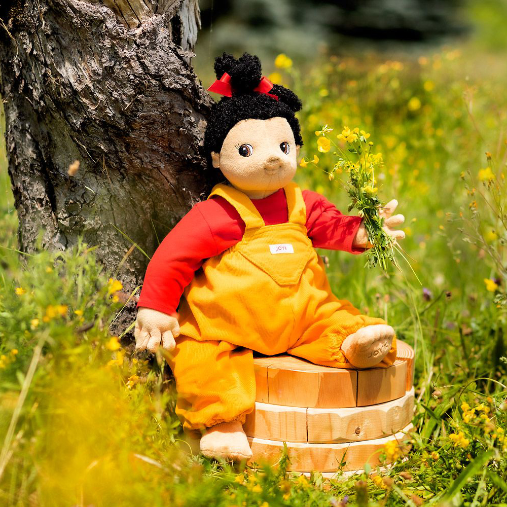 Joyk empathy doll Naomi sitting on a wooden tub in a flower meadow
