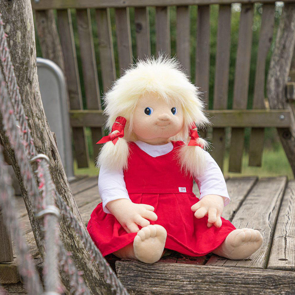 The Joyk empathy doll Nelly sitting on a wooden play tower