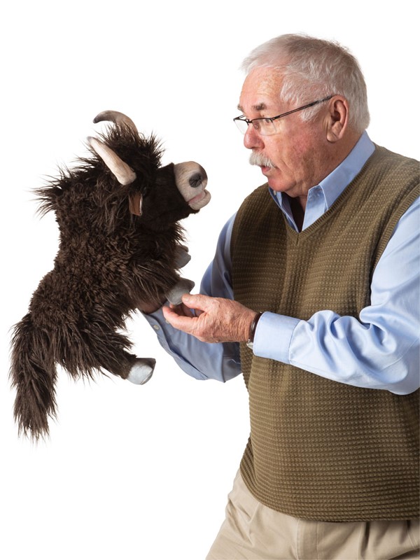 Older man operating the Folkmanis yak hand puppet with dark shaggy fur and horns, looking it directly in the face