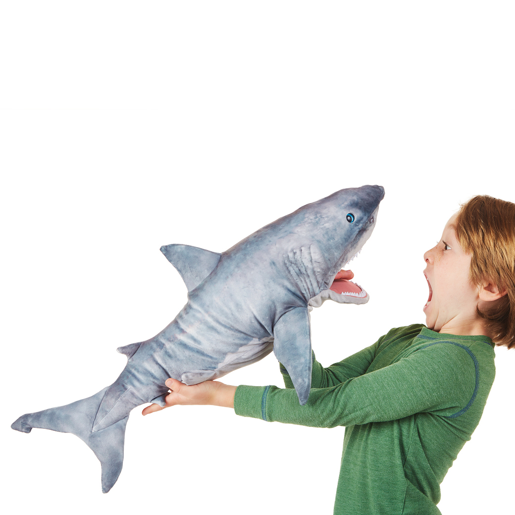 Boy holding a Folkmanis great white shark hand puppet with open mouth towards him, grey-white plush, side view