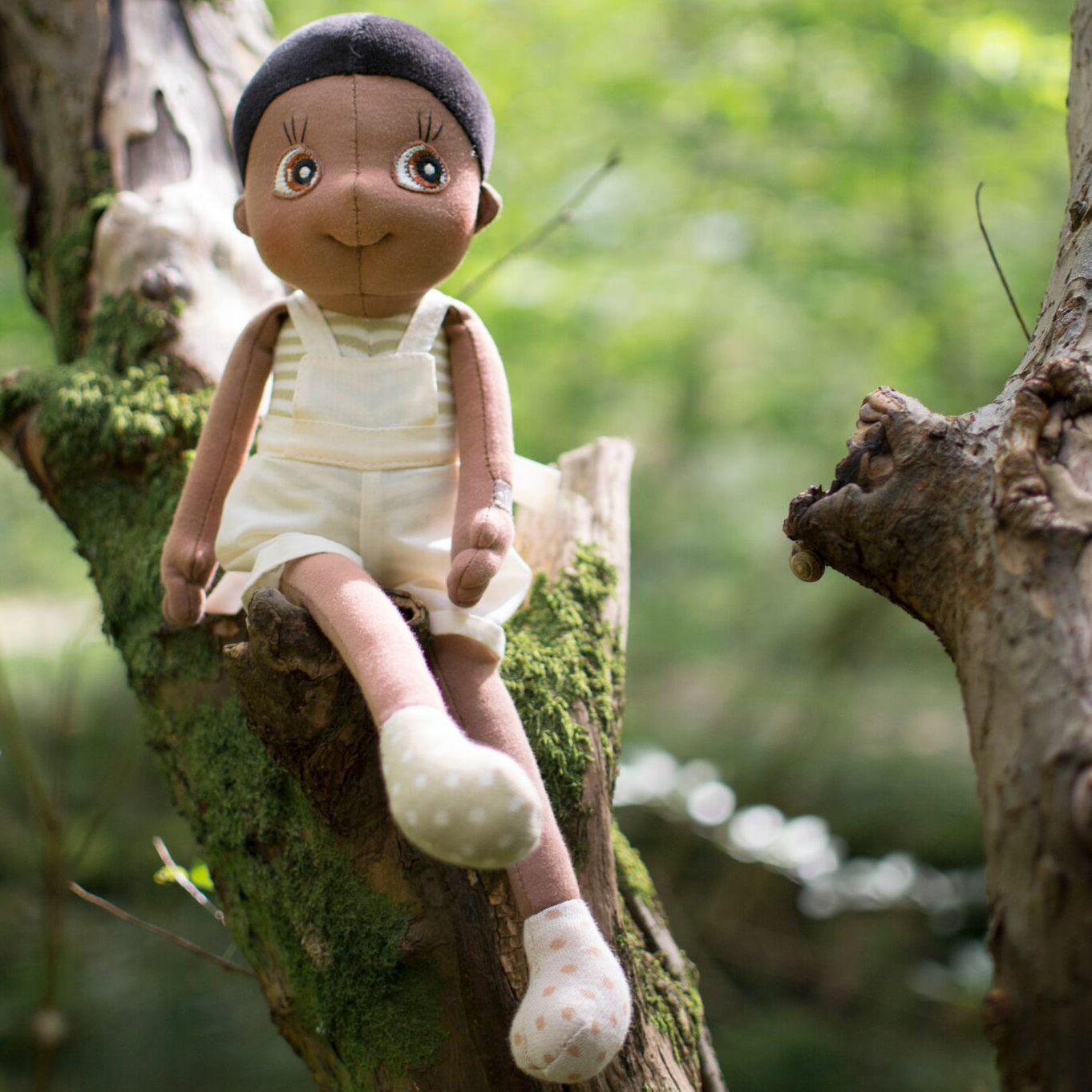 The Rubens EcoBuds doll Fern sitting on a mossy branch in the forest