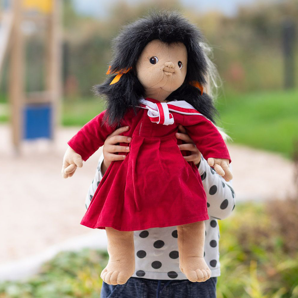 Child carrying the Joyk empathy doll Mia in a red dress on the playground