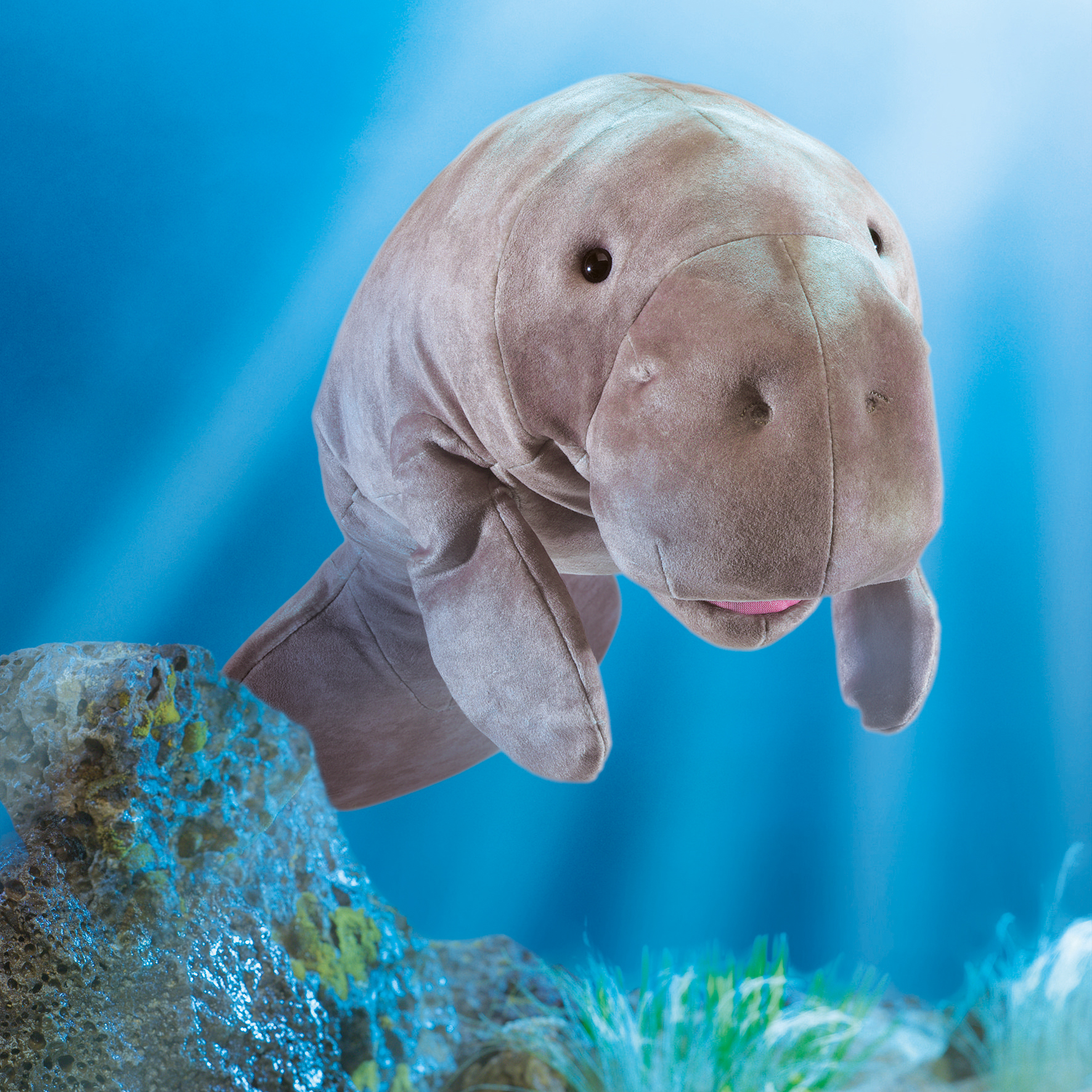 Folkmanis manatee hand puppet in grey plush with movable mouth, shown against a blue underwater background with rocks