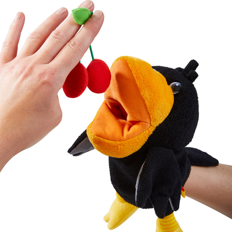HABA baby hand puppet raven Theo, close-up of a hand holding plush cherries to the raven's beak
