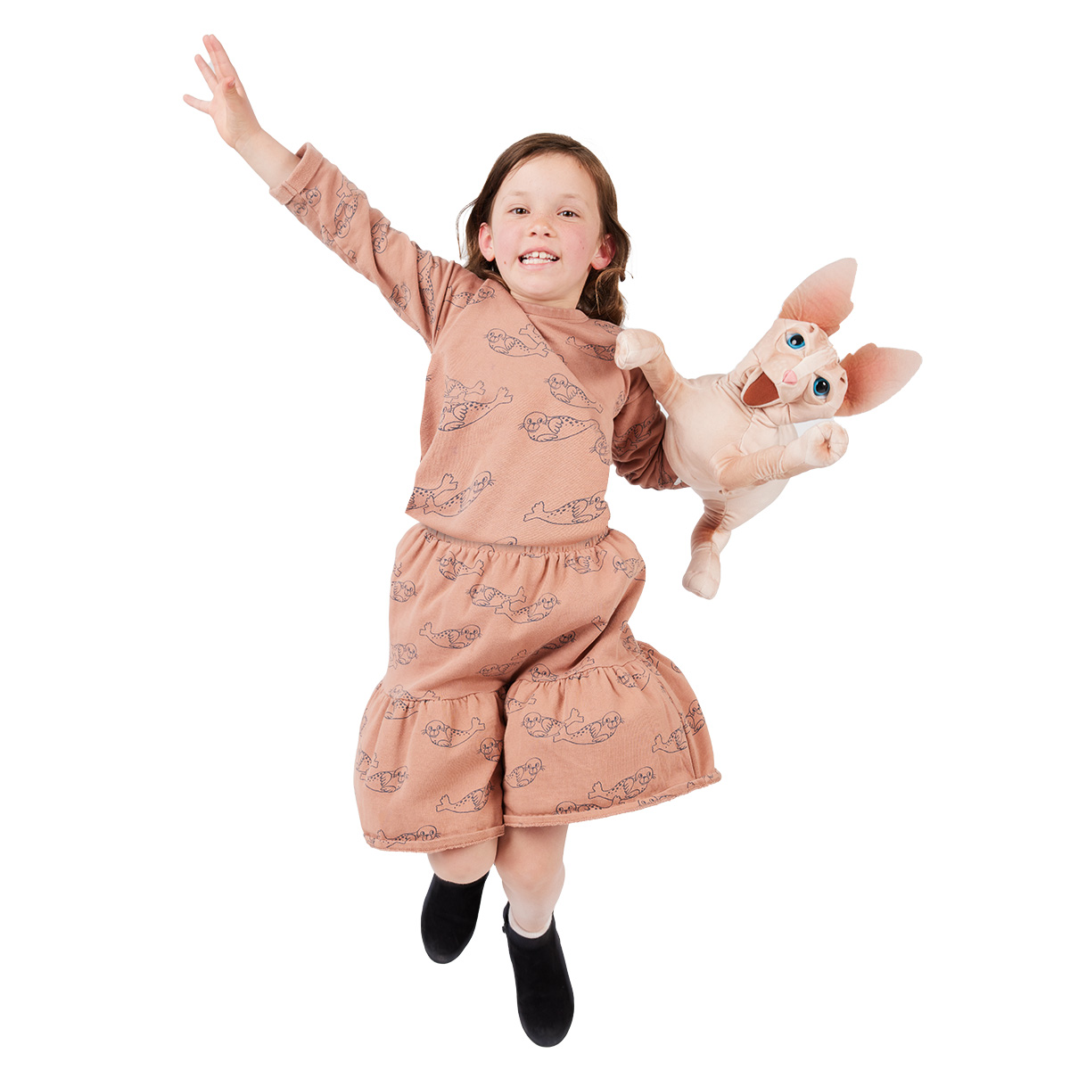 Girl jumping joyfully, holding a Folkmanis Sphinx cat hand puppet with large ears and blue eyes up in the air