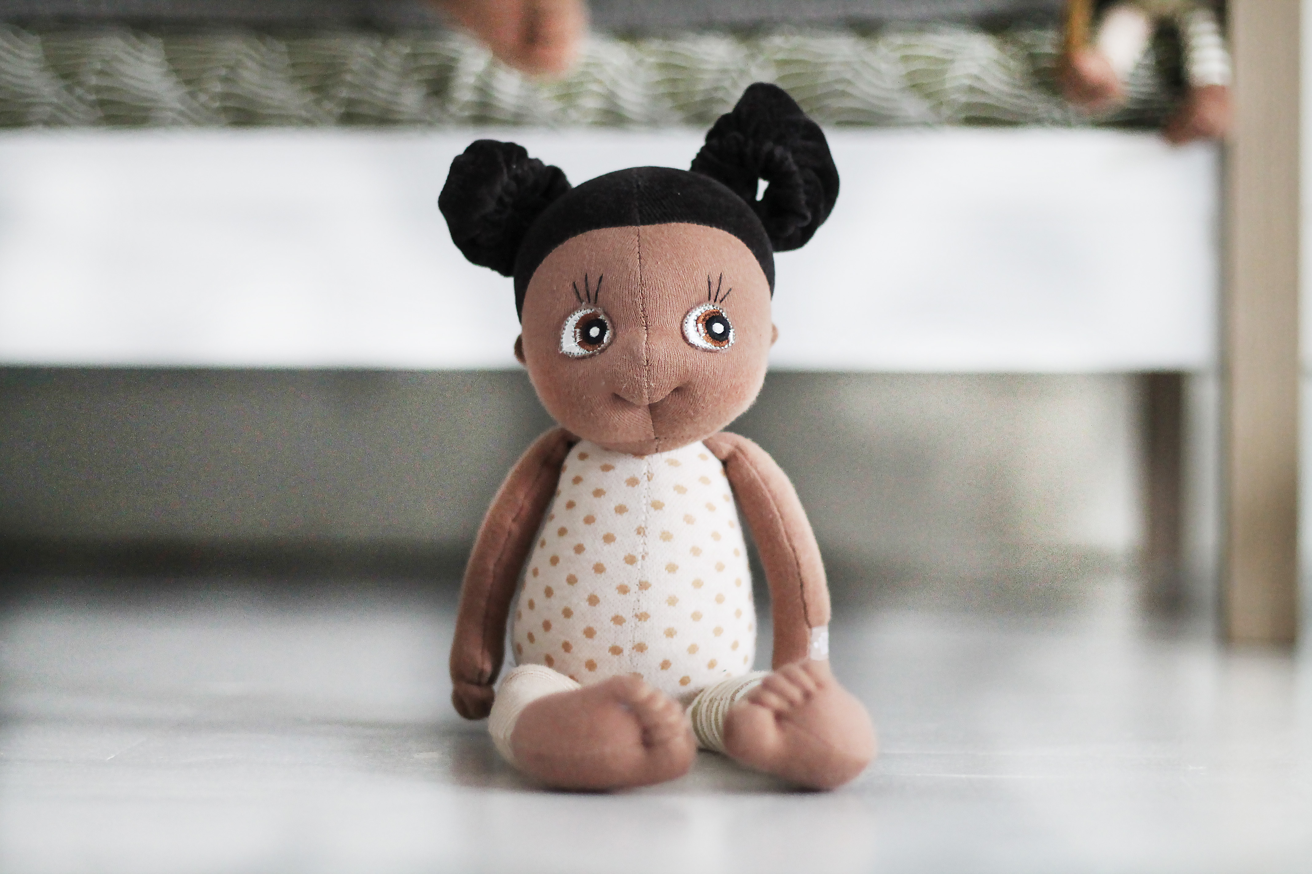 Rubens EcoBuds mini doll Flora sitting with dotted top in front of a bed