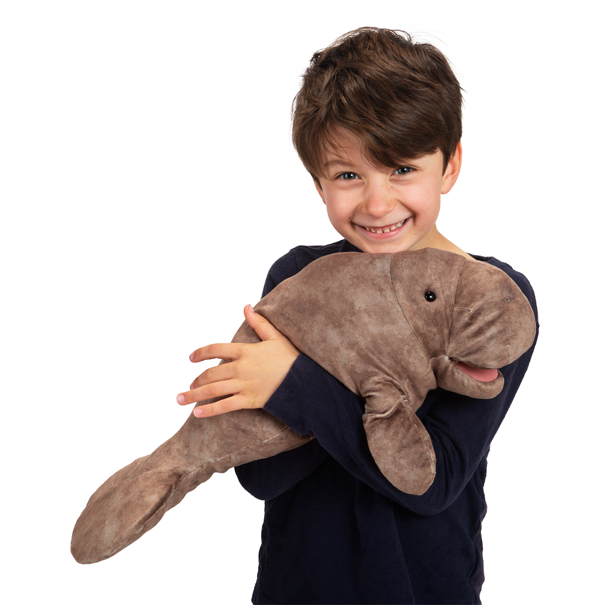 Smiling boy hugging the Folkmanis manatee hand puppet made of grey-brown plush with both arms