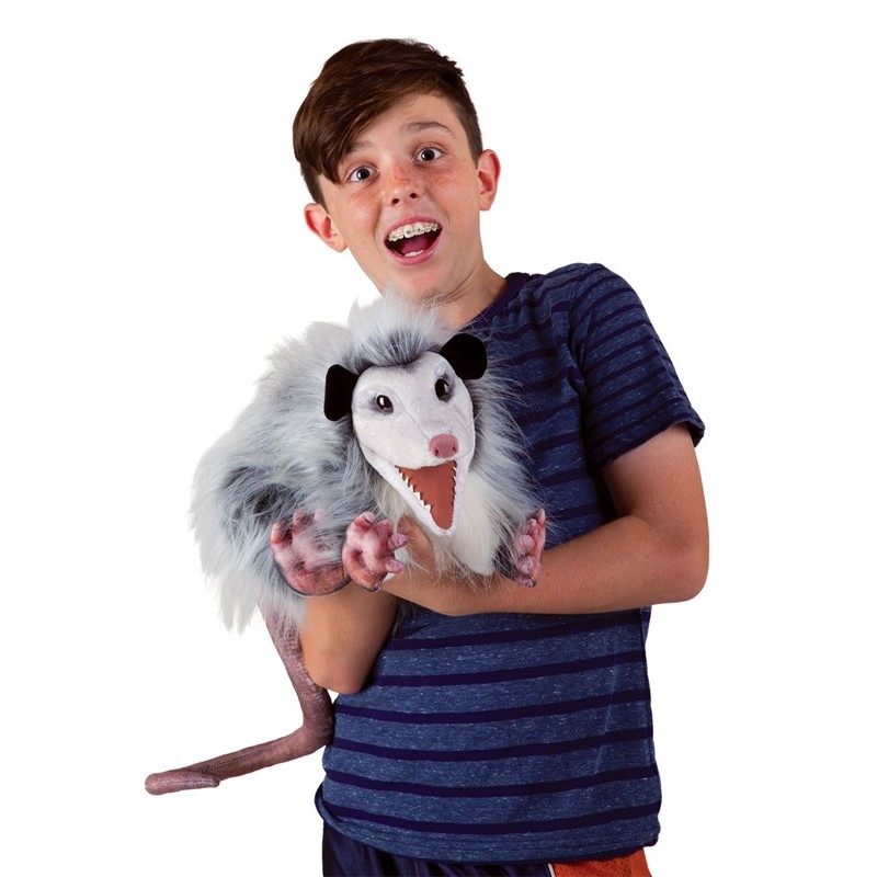 Boy holding a Folkmanis opossum hand puppet with an open mouth and shaggy grey-and-white fur in his arms
