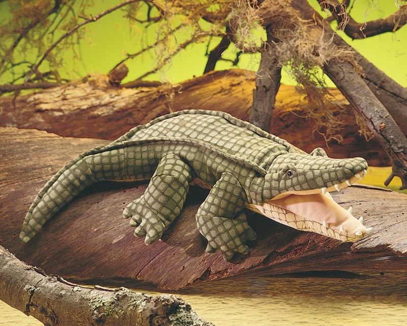 Folkmanis alligator hand puppet with open mouth and detailed green scale texture, lying on a tree trunk