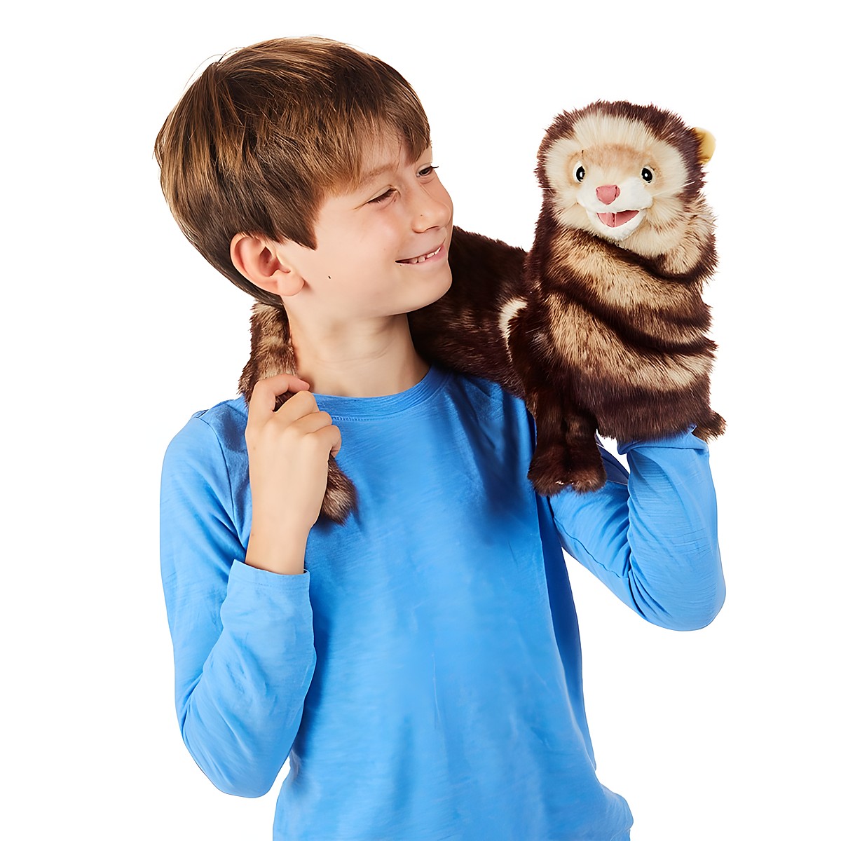 Boy holding a Folkmanis ferret hand puppet with brown fur and open mouth on his right hand, tail draped over his shoulder