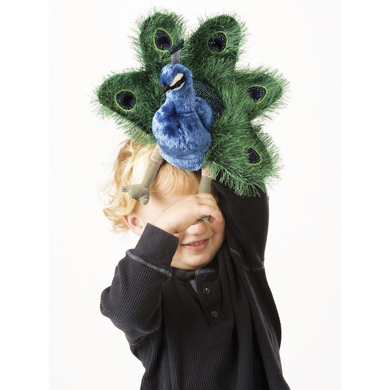 Child holding a Folkmanis small peacock hand puppet in front of their face, with blue plumage and a green fan of eye-spot feathers