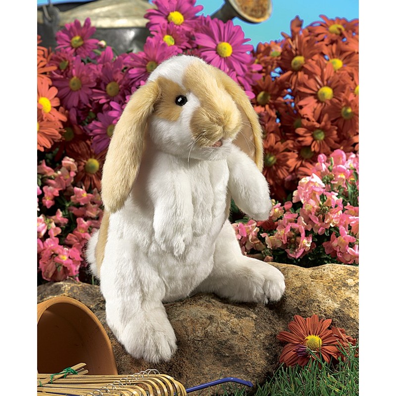 Folkmanis hand puppet standing lop rabbit with white plush fur and beige floppy ears, upright on a stone in front of a floral background