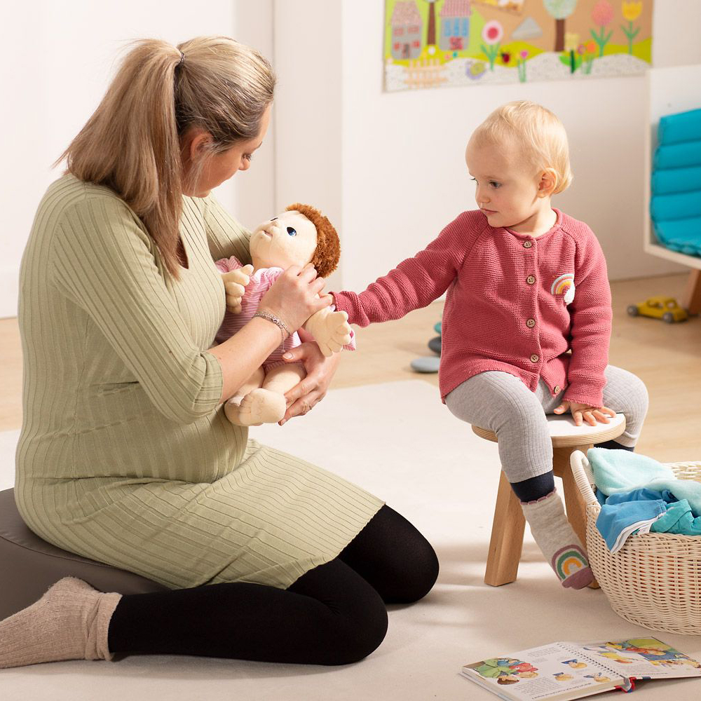 Woman and toddler looking at the Joyk empathy doll Baby Lilly in a playroom