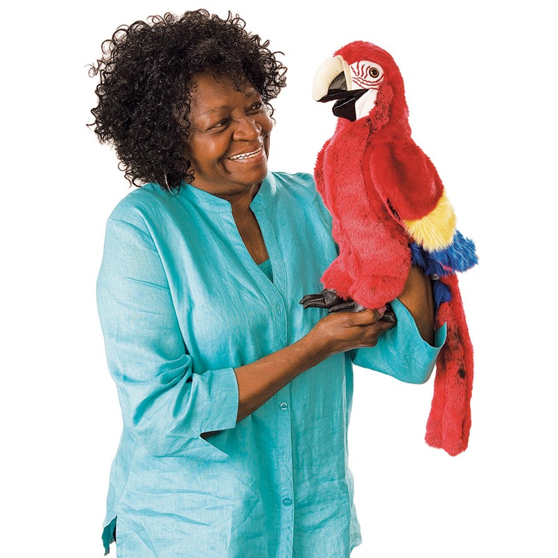 Folkmanis scarlet macaw hand puppet in vibrant red with yellow-blue wings, held on the arm of a smiling woman