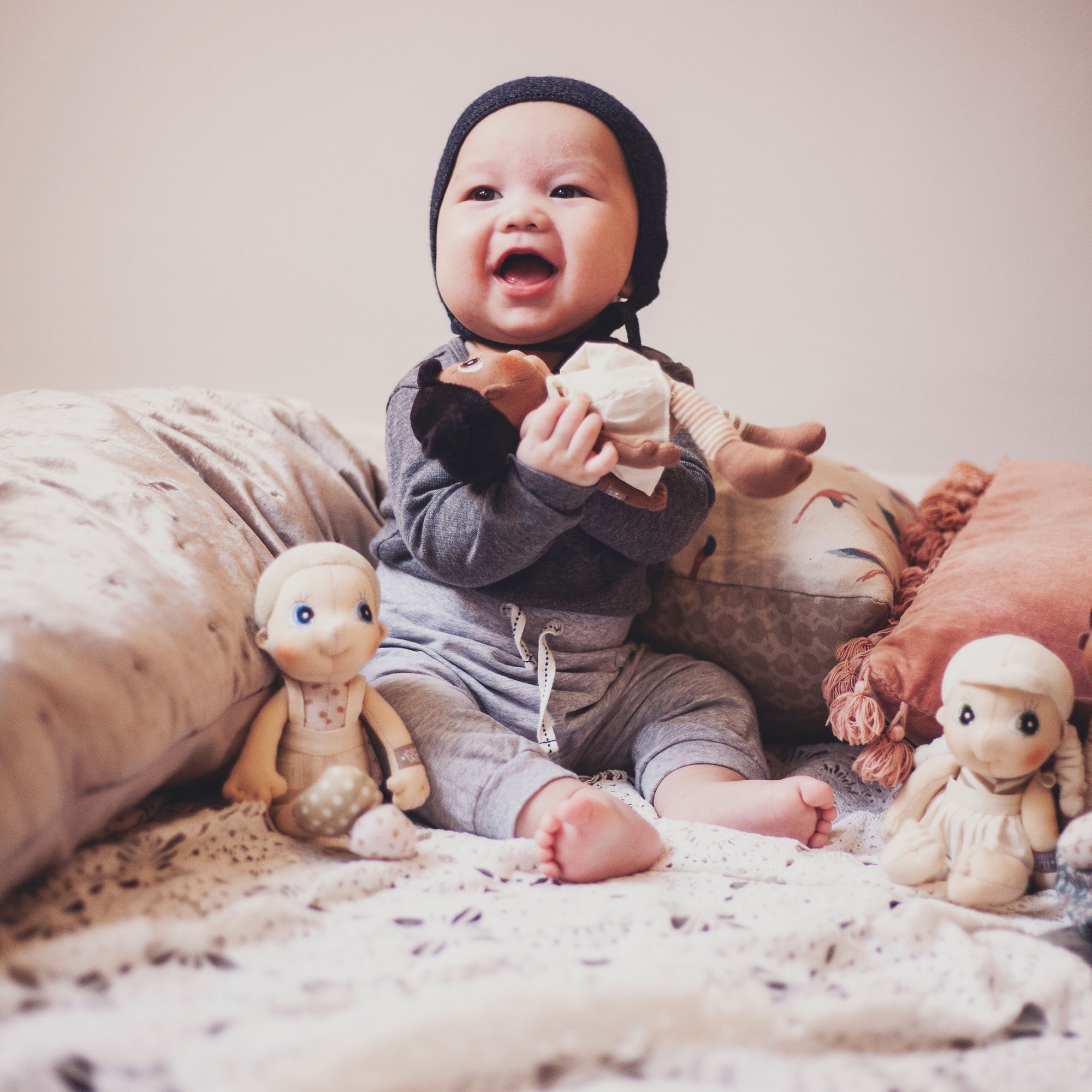Laughing baby with the Rubens EcoBuds mini dolls on the bed