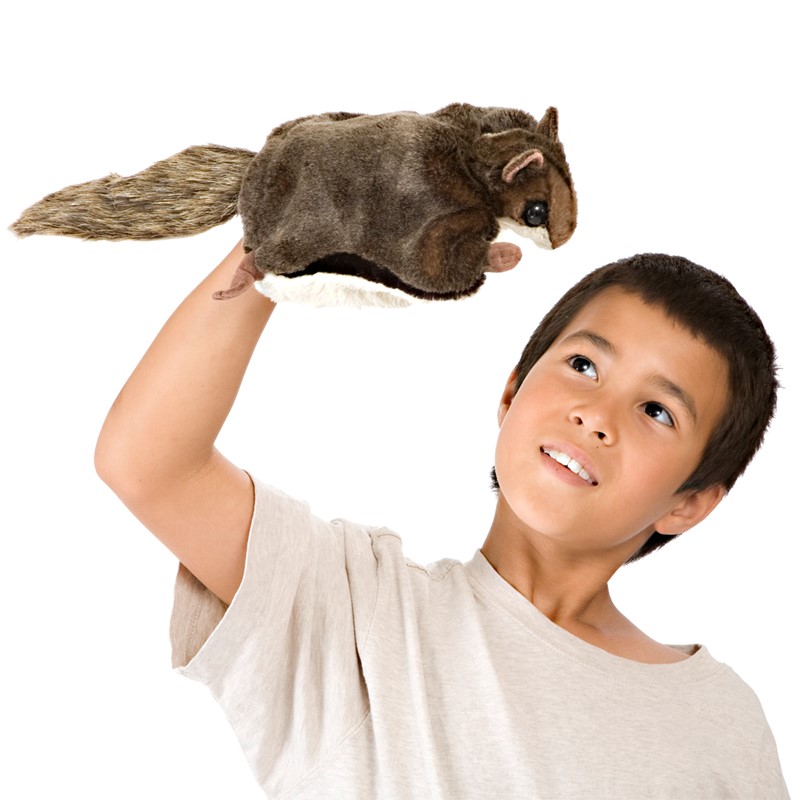 Boy holding a Folkmanis flying squirrel hand puppet with brown fur and a bushy tail high above his head