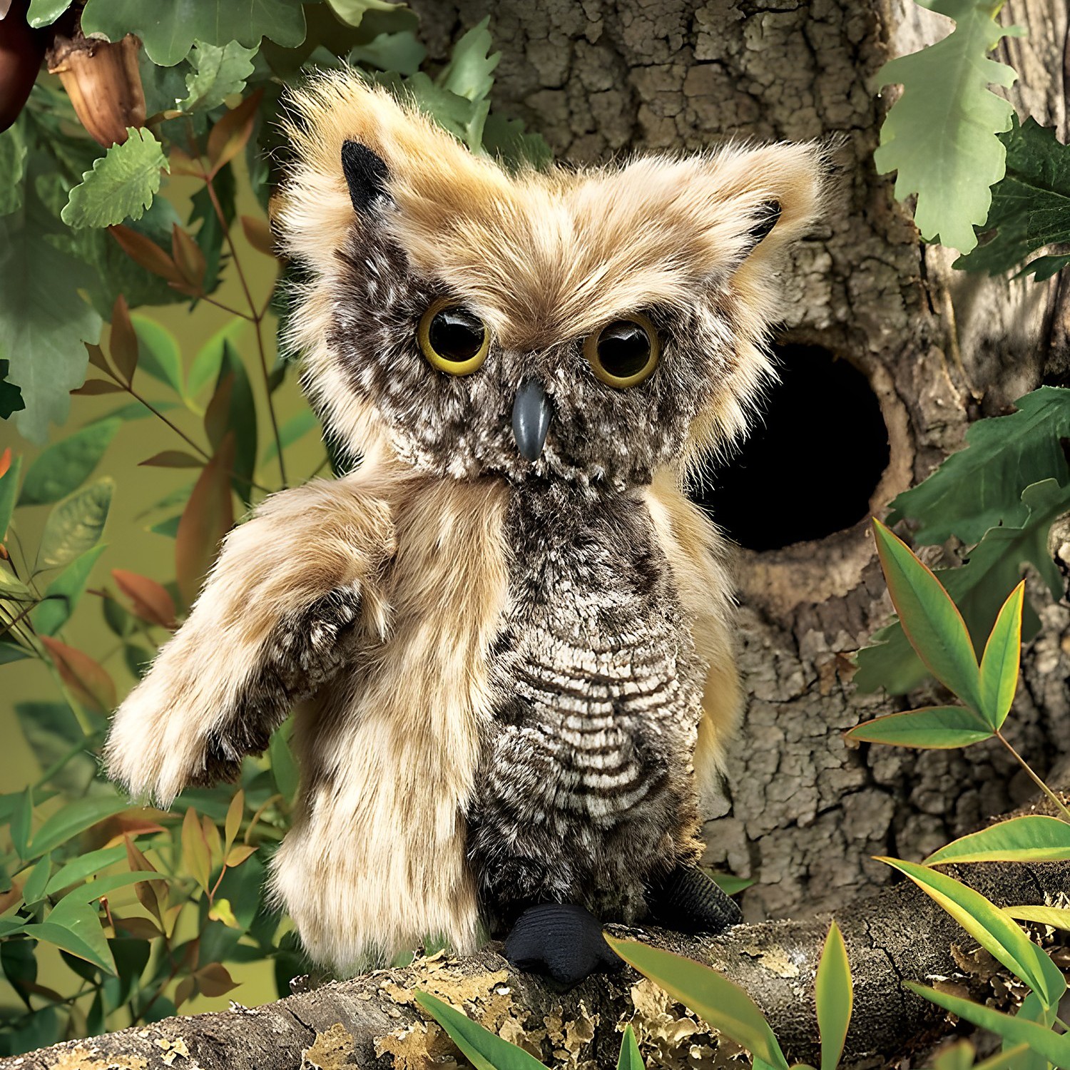 Folkmanis screech owl hand puppet with beige-brown plumage and yellow eyes, sitting on a branch in front of a tree hollow