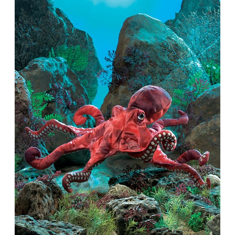 Folkmanis hand puppet red octopus with white suckers on eight tentacles, set against a staged ocean floor with rocks and seaweed