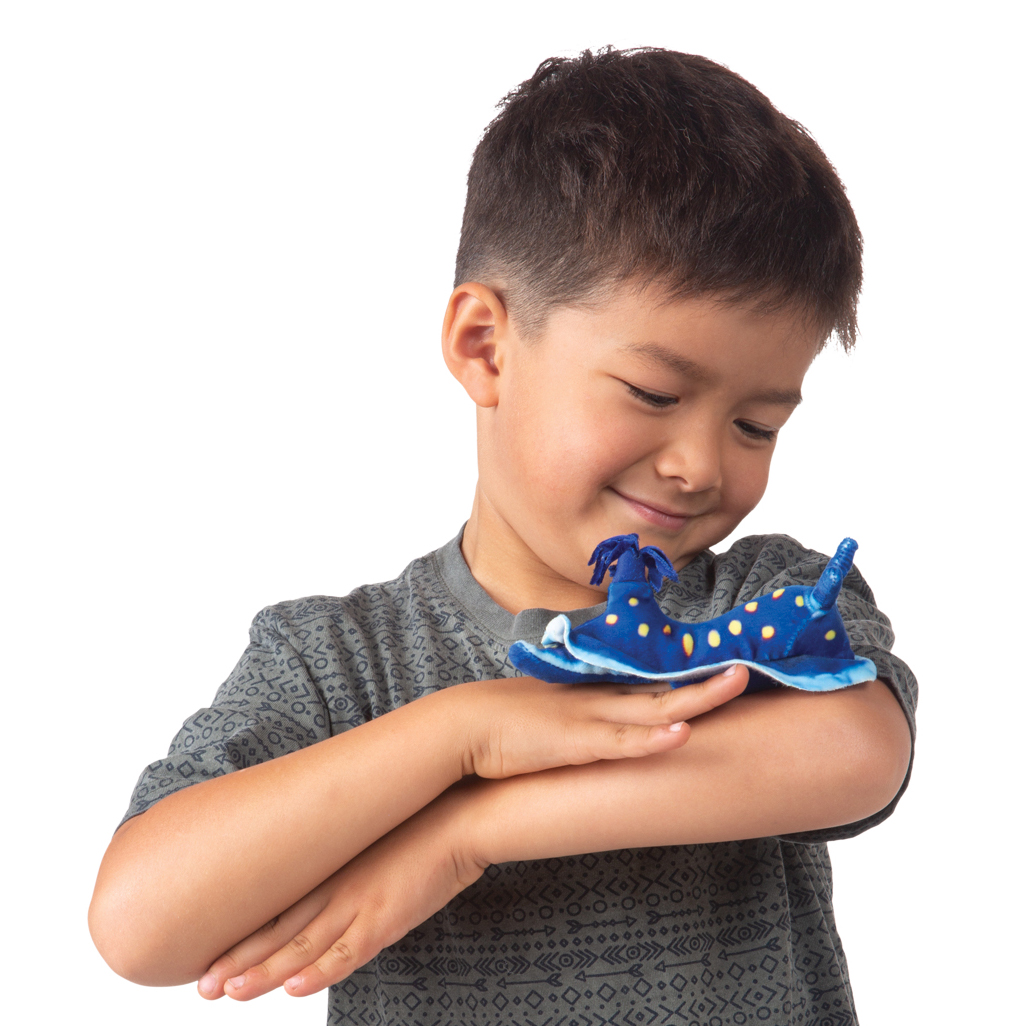 Boy smiling while holding a Folkmanis mini blue nudibranch finger puppet with yellow spots on the back of his hand