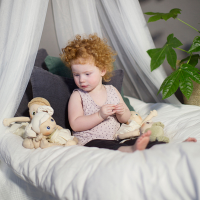 Child sitting with the Rubens EcoBuds dolls under a bed canopy