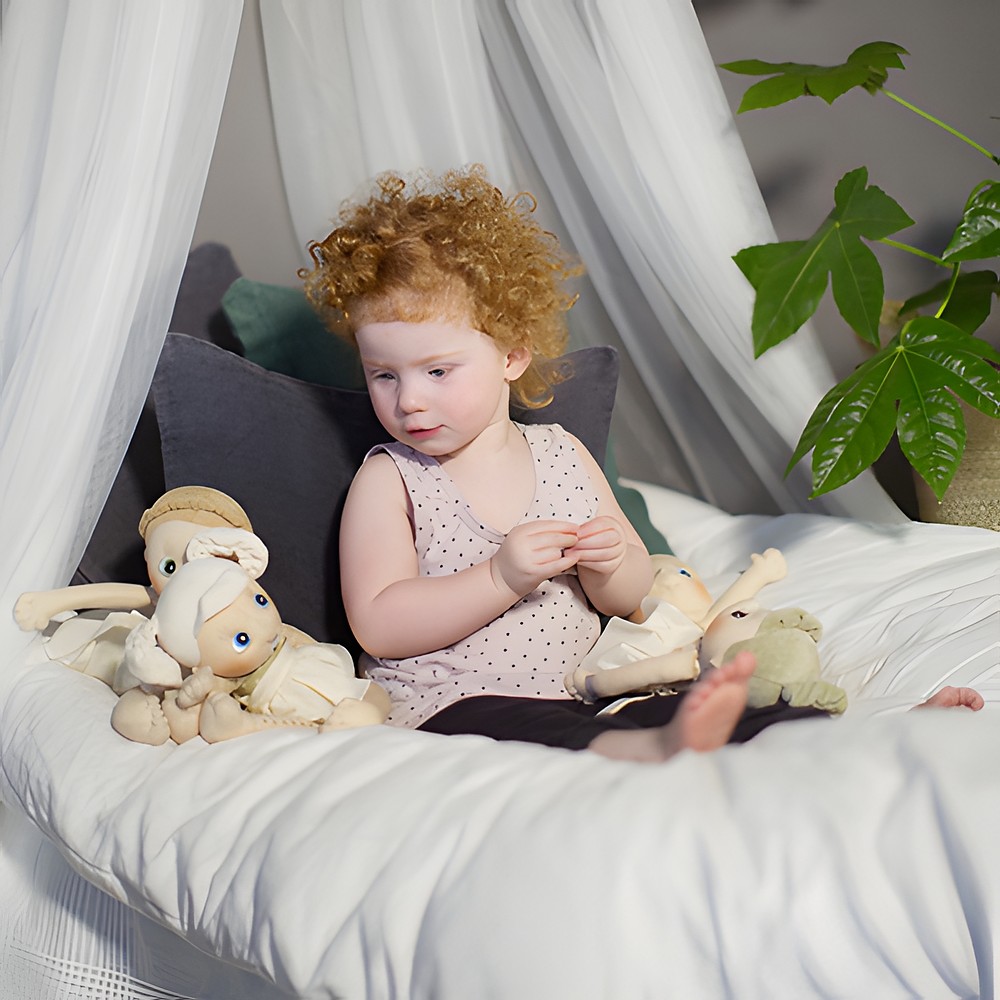 Child sitting with the Rubens EcoBuds dolls under a bed canopy