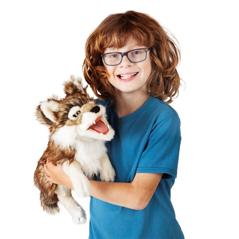 Laughing boy with glasses holding the Folkmanis grey wolf hand puppet with open mouth and brown-beige fur against a white background
