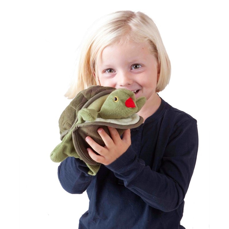 Smiling child holding the Folkmanis baby turtle hand puppet with a green head and red mouth in both hands